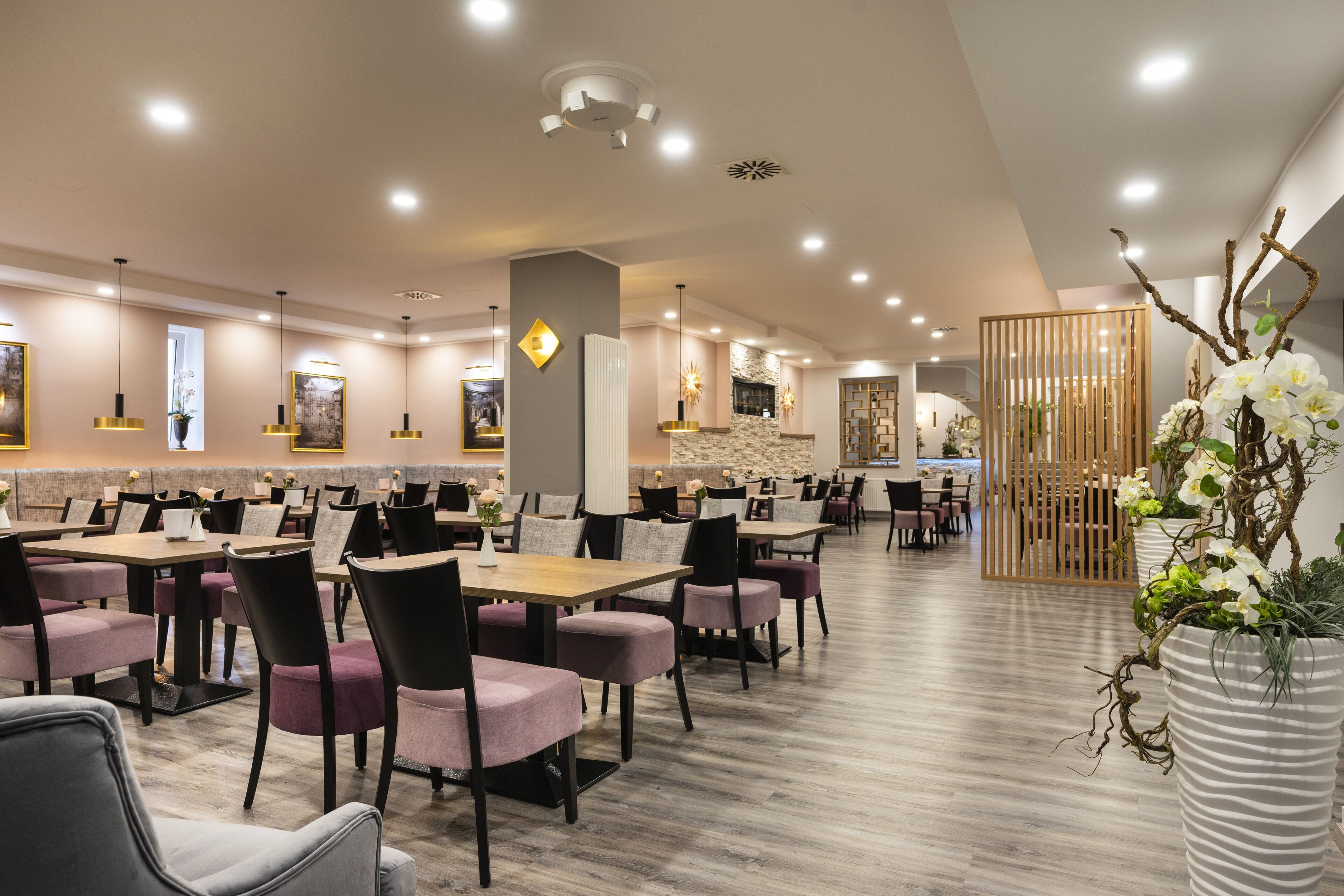 A modern dining area with multiple tables and chairs, recessed ceiling lighting, and decorative wall art.