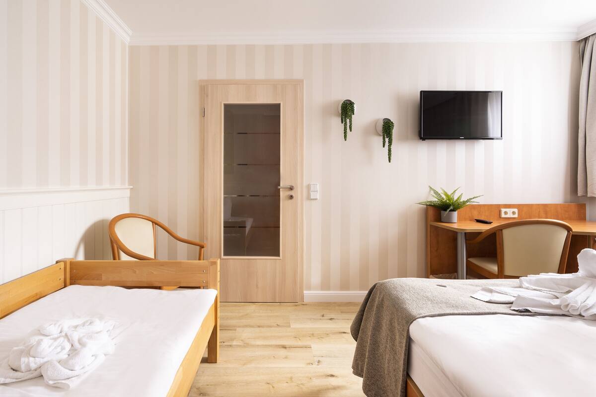 A hotel room with two single beds, a desk, a chair, a TV, and a wardrobe.