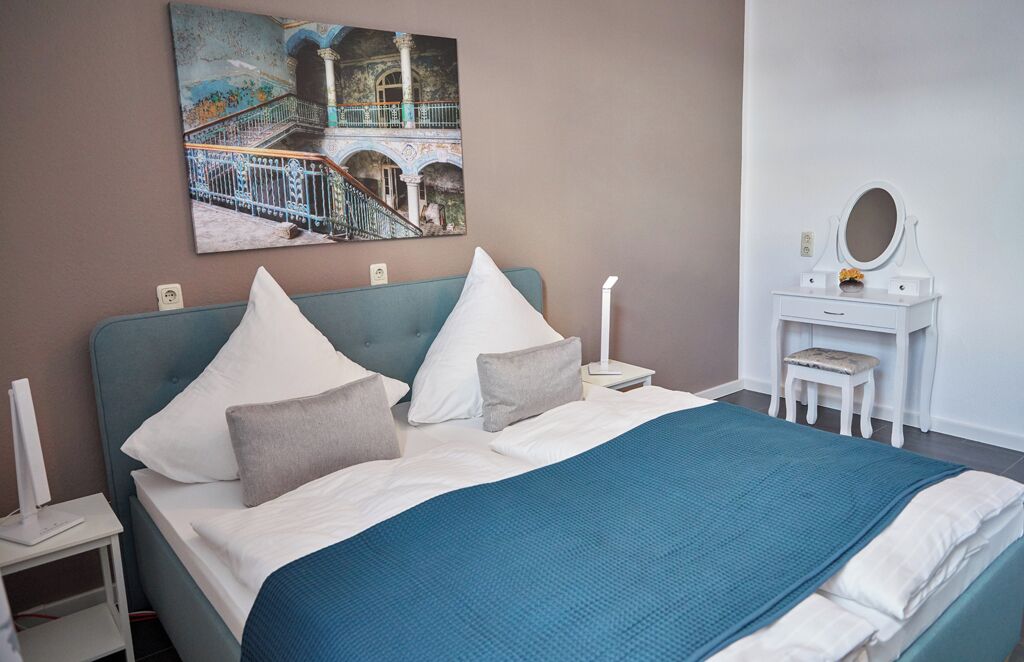 A bedroom with a bed, a nightstand, a dresser, a mirror, and a painting on the wall.