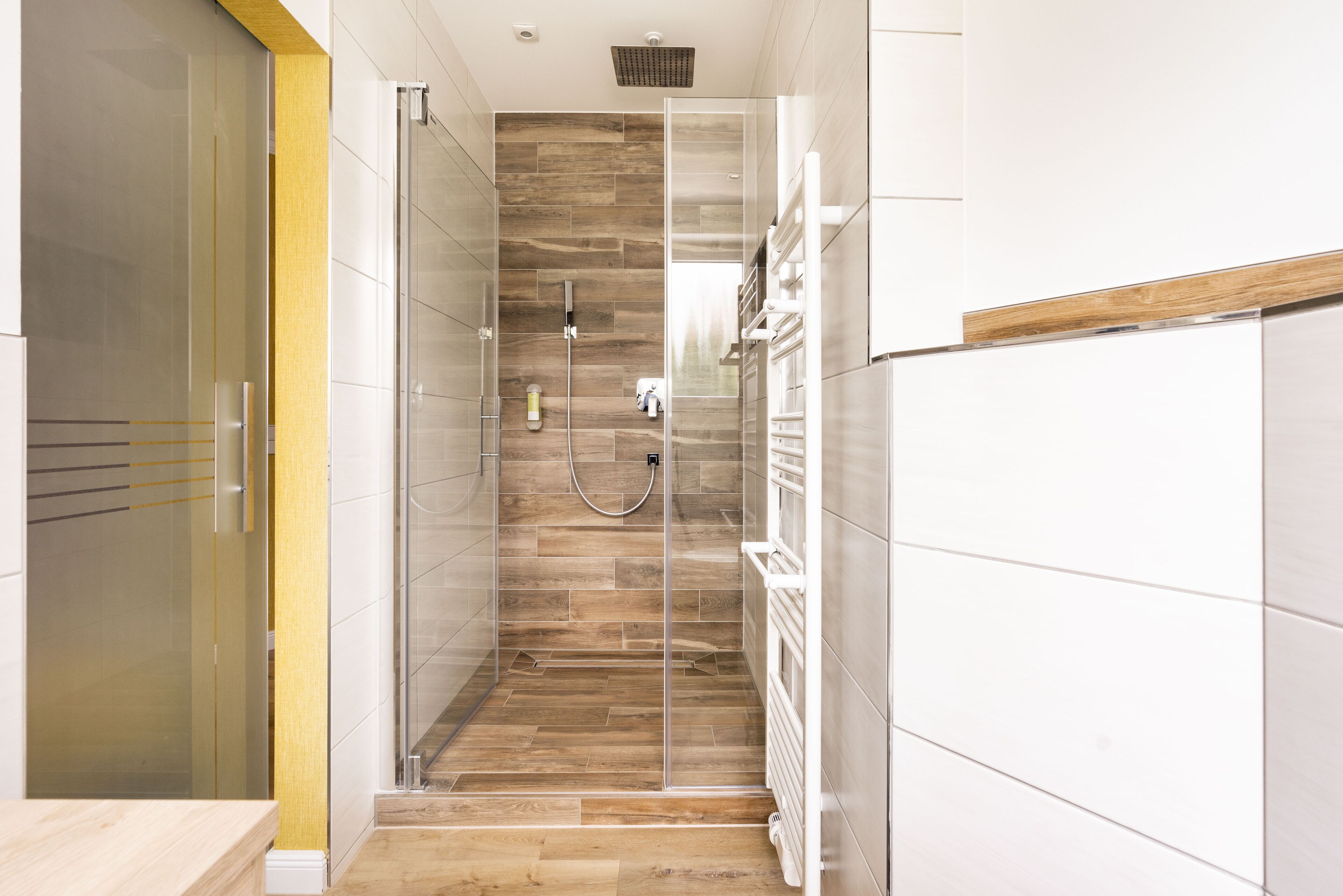 Un baño moderno con cabina de ducha de vidrio, suelo de madera y paredes de azulejos blancos.