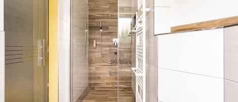 Un baño moderno con cabina de ducha de vidrio, suelo de madera y paredes de azulejos blancos.