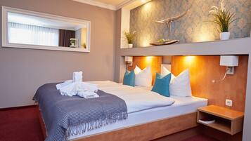 Hotelkamer met een groot bed, een houten hoofdbord, een nachtkastje, een spiegel, een raam met gordijnen en een wandplank met planten.