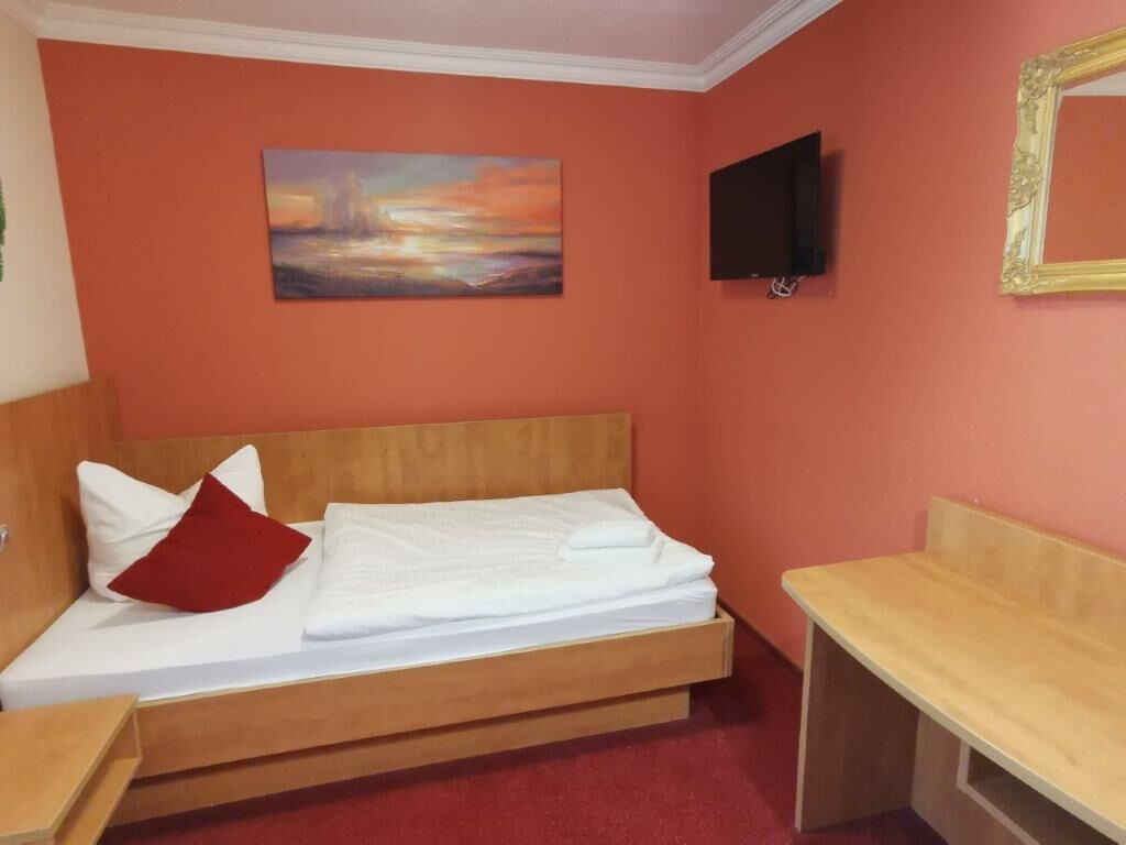 A room with a bed, a TV, and a painting on the wall.