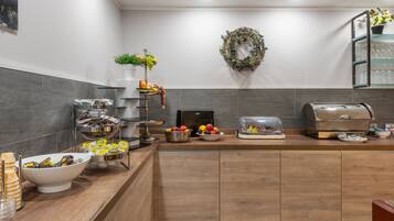A modern kitchen with a wooden countertop, a coffee station, a fruit display, and a decorative wreath on the wall.