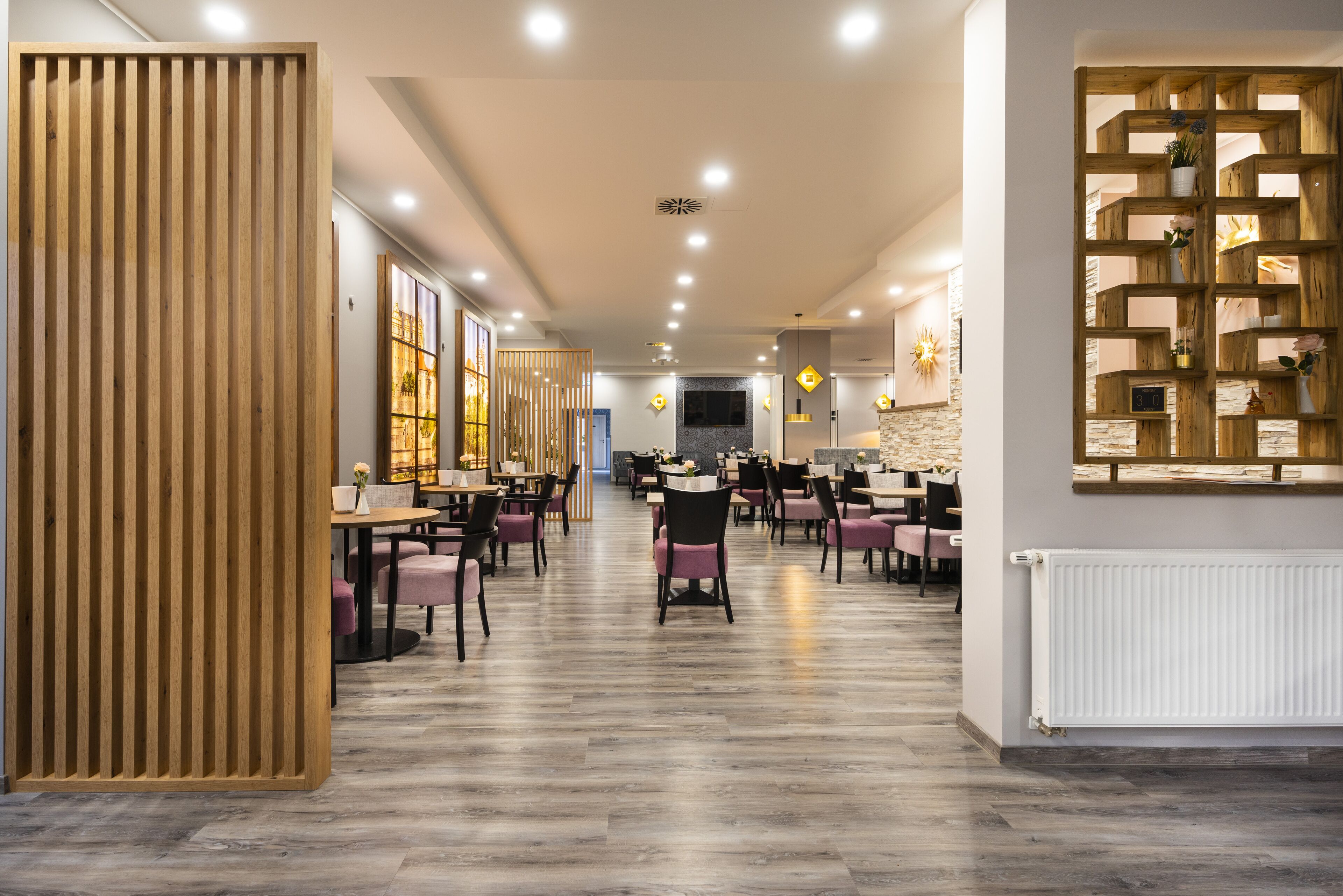 A modern restaurant with wooden panel dividers, a central seating area with tables and chairs, and a decorative wall with shelves.