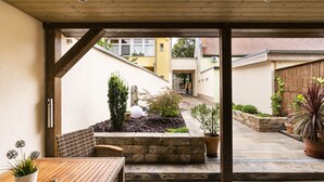 An outdoor patio area with a wooden table and chairs, stone planters, and a small garden. - Cityhotel Bernburg (Bernburg)