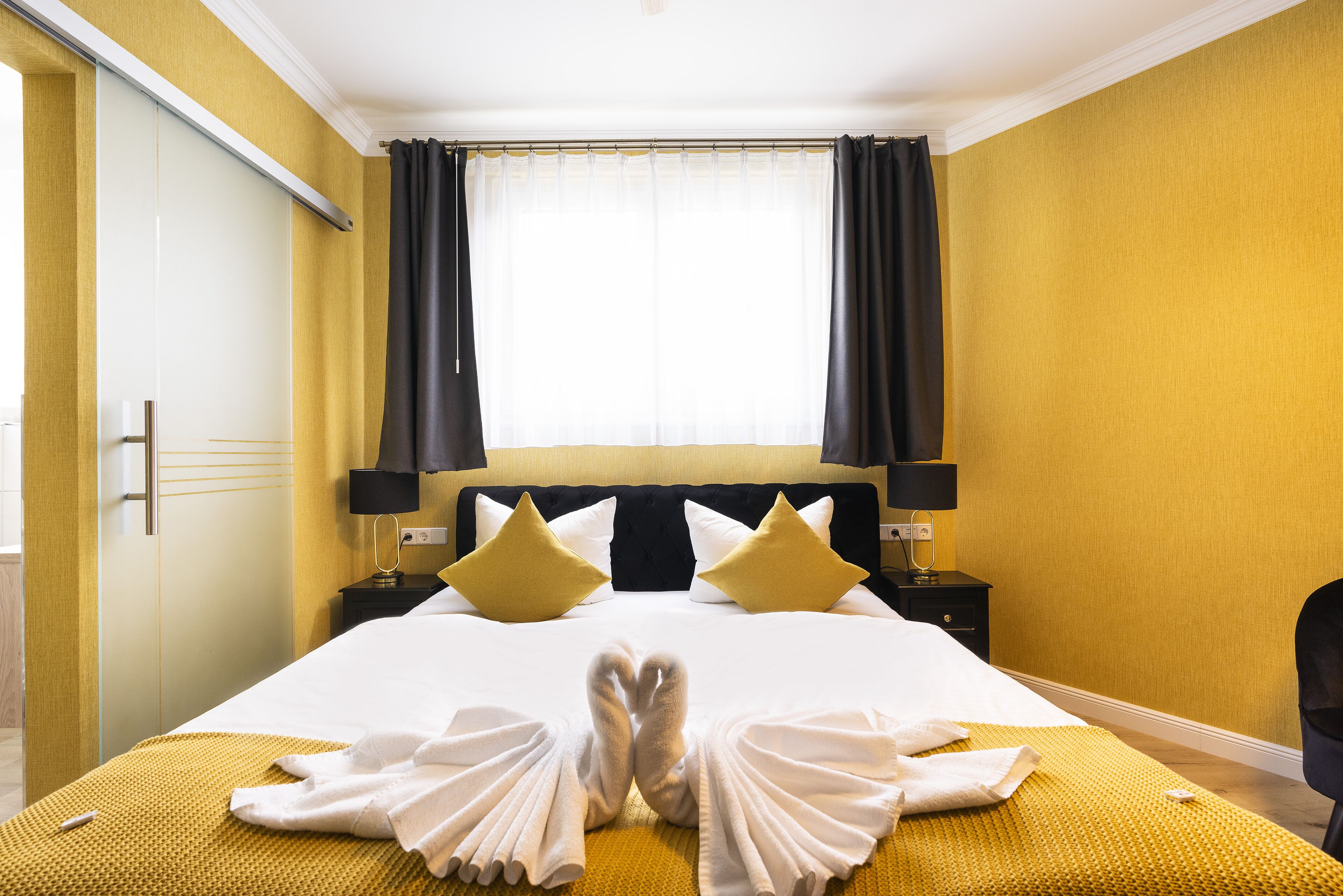 Ein Hotelzimmer mit einem großen Bett, zwei Nachttischen, einem Fenster mit Vorhängen.