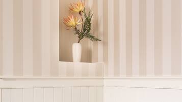 Una cama individual con estructura de madera y ropa de cama blanca, un almohadón blanco y un pequeño florero con flores en la pared de arriba.