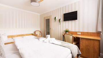 A hotel room with a bed, a desk, a chair, a television, and a ceiling fan.