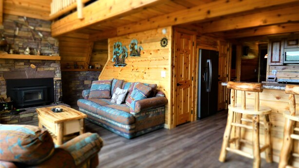 Interior acolhedor de uma cabana com lareira, sofá, área de jantar e geladeira.