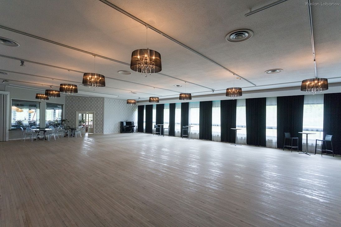 A spacious room with a wooden floor, large windows, and multiple chandeliers.