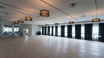 A spacious room with a wooden floor, large windows, and multiple chandeliers.