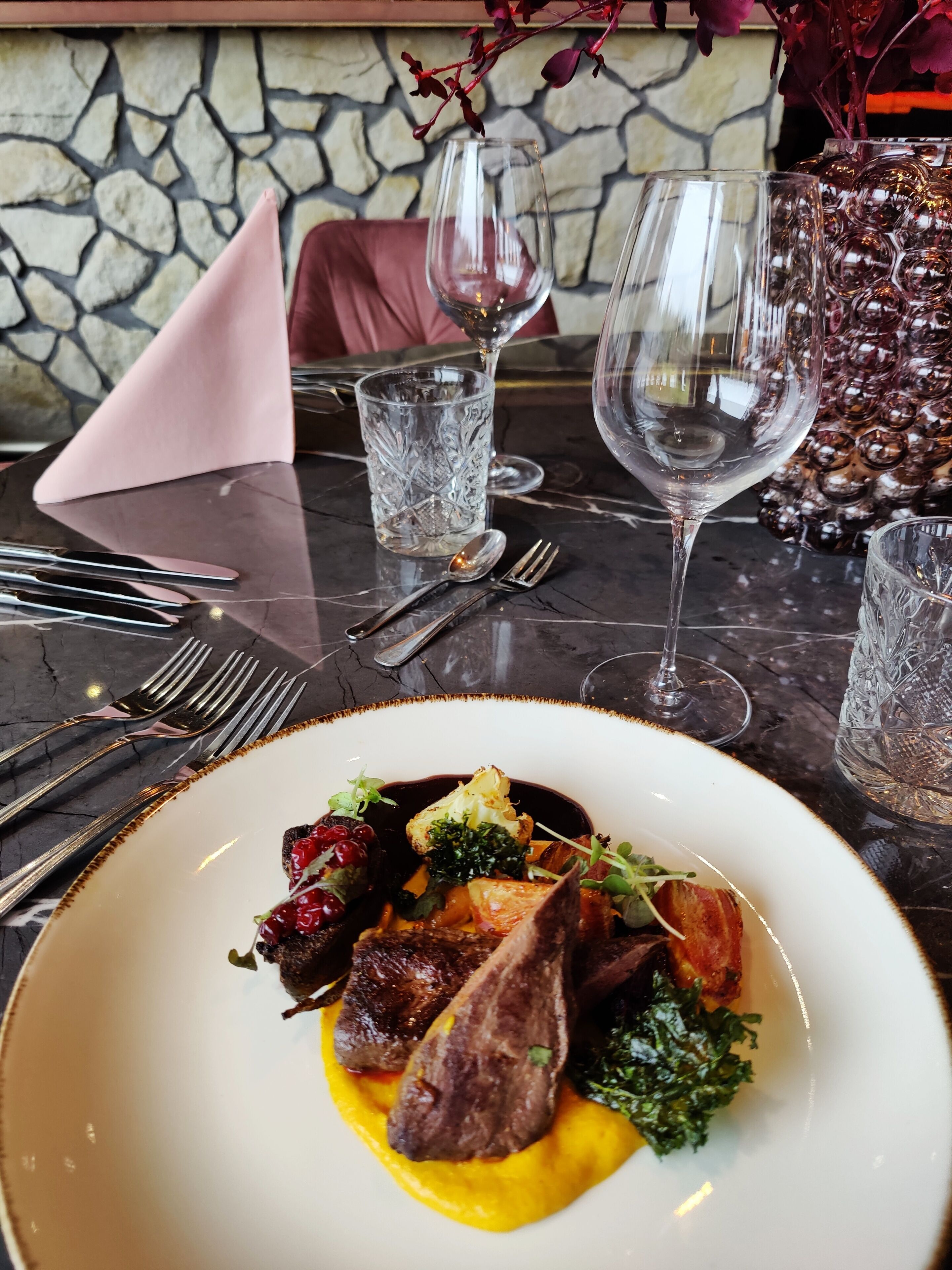 Una mesa de comedor con un plato de comida, cubiertos y copas de vino.
