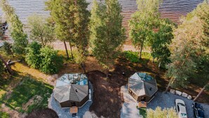 An aerial view of a lakeside property with two cabins, surrounded by dense trees and a sandy beach. - Revontuli Resort Glass Igloos (Hankasalmi)