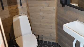 Un baño pequeño de madera con inodoro blanco, lavamanos y repisas con toallas dobladas.