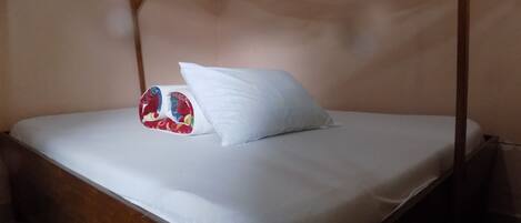 Una cama individual con colchón y almohadas blancas, y un mosquitero sobre un marco de madera.