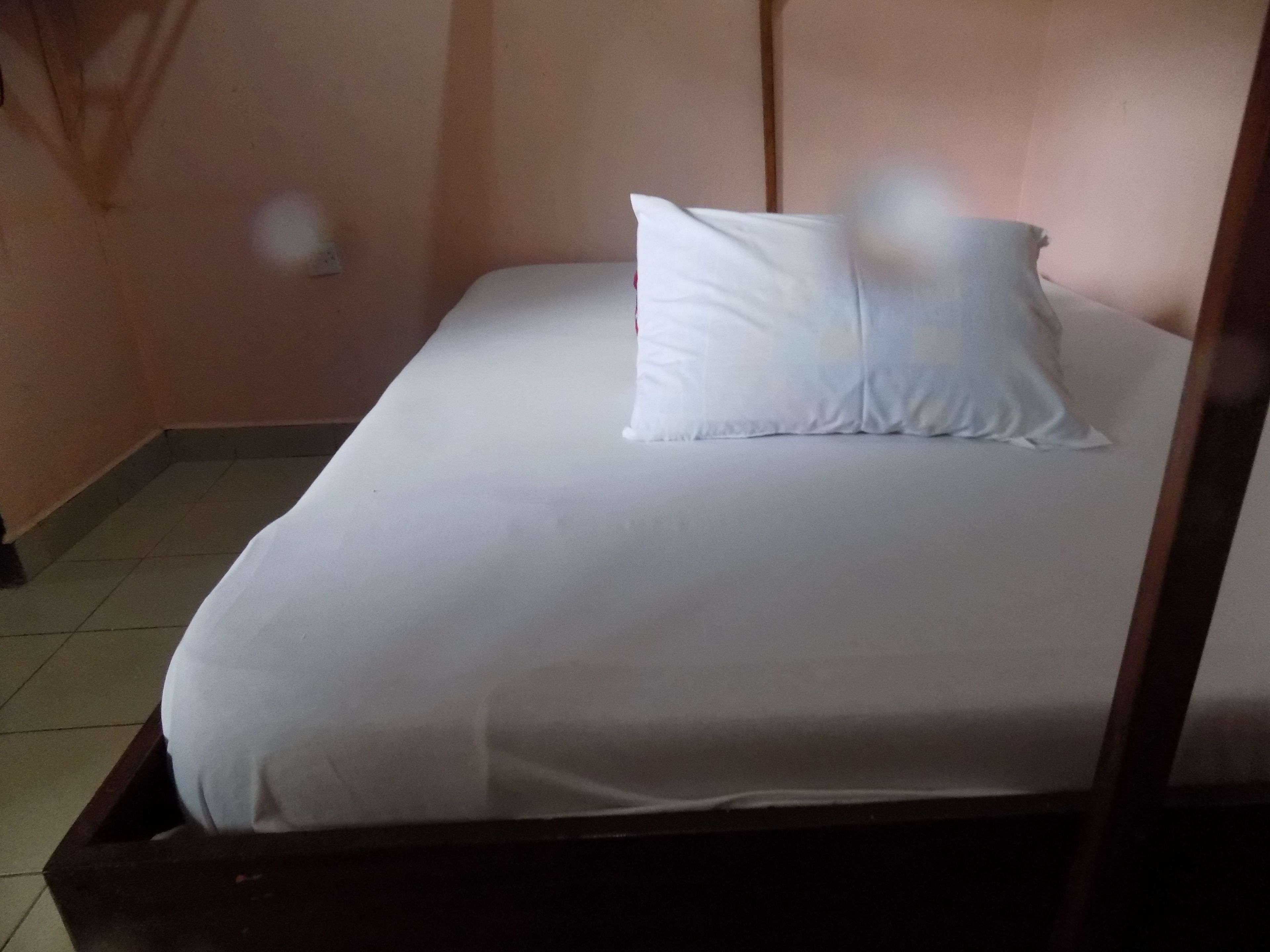 Una cama individual con ropa blanca en una habitación con paredes lisas y piso de baldosas.