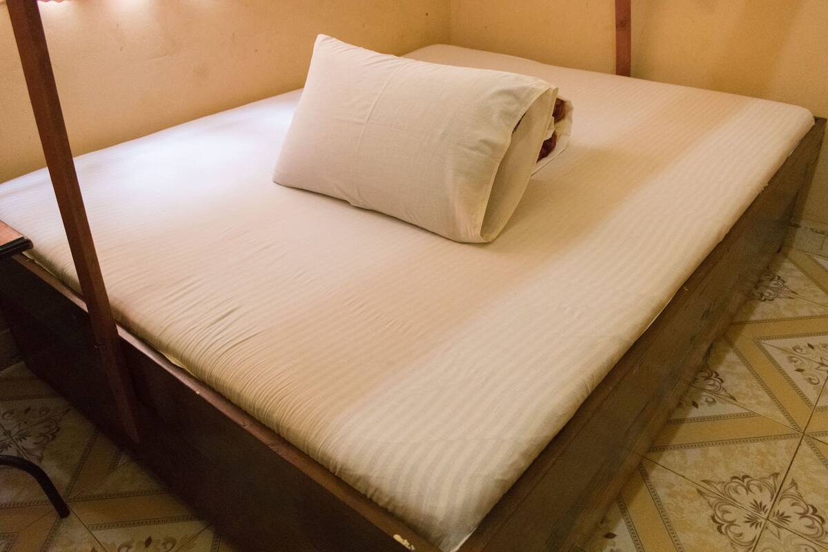 A single bed with a wooden frame, a white mattress, and a white pillow.