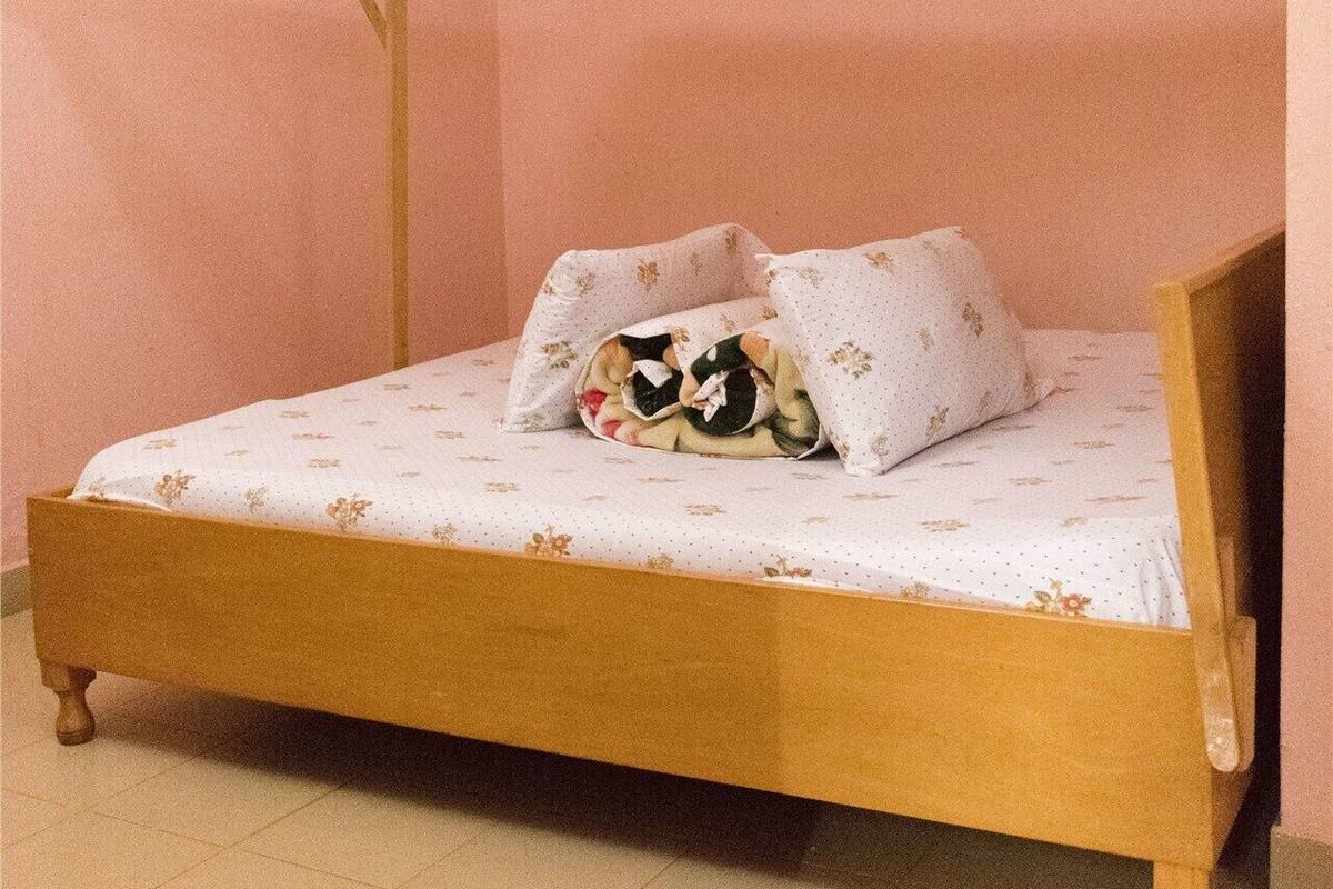 A single bed with a canopy, a floral-patterned bedspread, and a pillow with a green and white design.