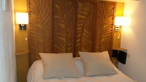 Un lit double avec deux oreillers, une tête de lit en bois ornée d’un motif de feuilles et deux lampes de chevet.
