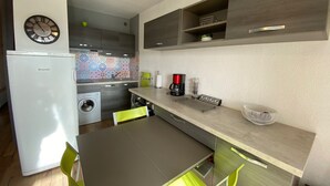 Une petite cuisine équipée d’un réfrigérateur, d’un lave-linge et d’une horloge murale.