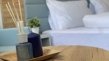 Een houten dienblad met een glazen vaas en rietverspreider op een tafel, een blauwe bank en een bed met witte beddengoed op de achtergrond.