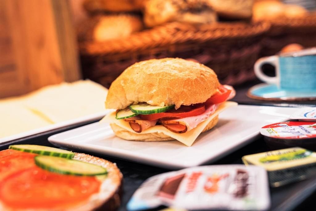 A sandwich on a plate with a cup and condiments in the background.