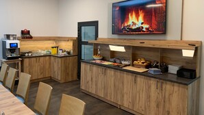 A modern kitchen with a built-in coffee machine, a TV displaying a fireplace, and a buffet counter with various food items. - besttime Hotel Monschau (Monschau)