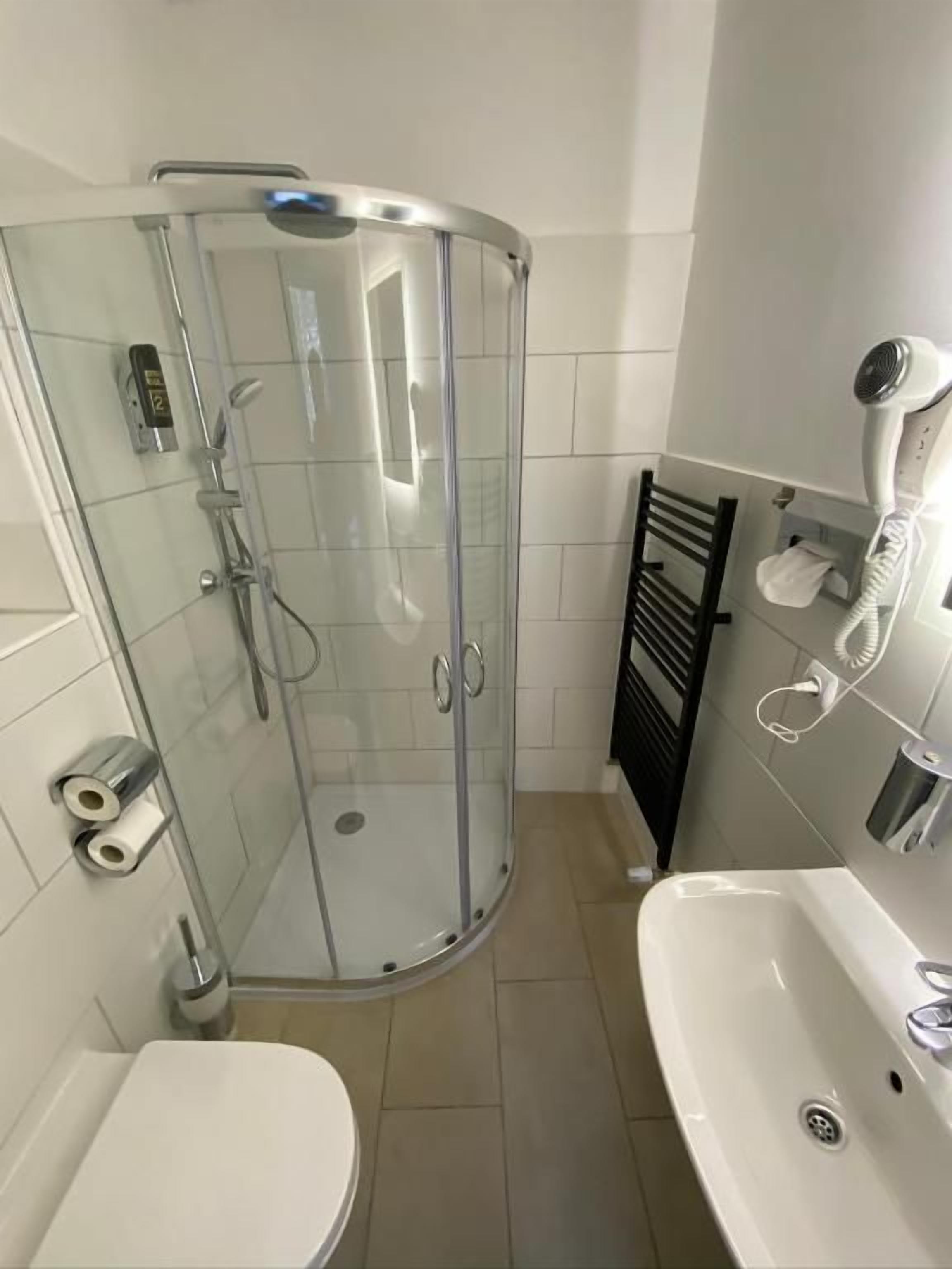A bathroom with a glass shower enclosure, a white sink, and a hairdryer on the wall.