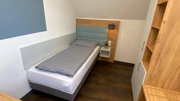 Una camera da letto piccola e moderna con un letto singolo, un comodino e scaffali a muro in legno.