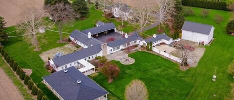 An aerial view of a large estate with multiple buildings, expansive green lawns, and a well-maintained orchard.