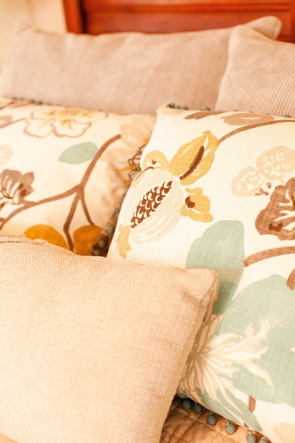 Primer plano de una cama con almohadas estampadas con motivos florales y una manta texturizada.