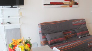 A living room with a grey sofa, a flat-screen TV, a painting on the wall, and a table with a vase of flowers. - Cozy apartment near thermal baths, pets allowed (Balaruc-les-Bains)