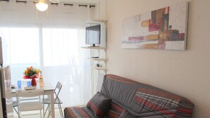 A modern living room with a sofa, a dining table with chairs, a TV on a stand, and a painting on the wall. - Cozy apartment near thermal baths, pets allowed (Balaruc-les-Bains)