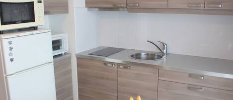 Una cocina compacta con microondas, pileta y muebles de madera.