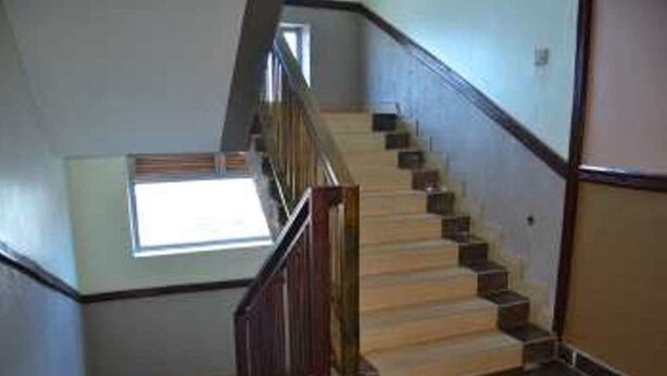 Un escalier avec des marches en bois et une rampe en métal, menant à un palier doté d’une fenêtre.