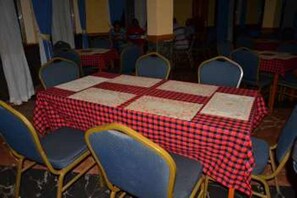 A dining area with tables covered in red and white checkered tablecloths, blue chairs, and a tiled floor. - Hilltop Hotel (Mbale)