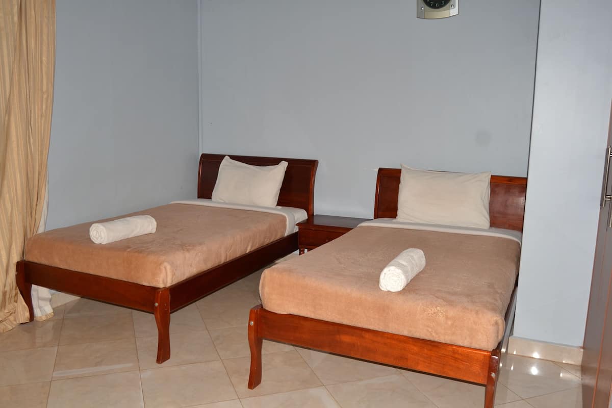 Two single beds with wooden frames and beige bedding, a clock on the wall, and a door to the right.