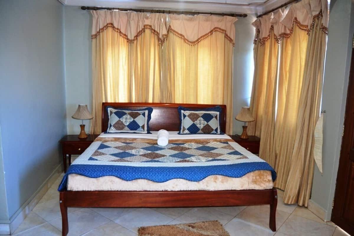 A bedroom with a wooden bed, a quilt, two bedside tables with lamps, and curtains.
