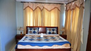Une chambre à coucher avec un lit en bois, deux tables de chevet, une couette bleue et blanche, et des rideaux beige.