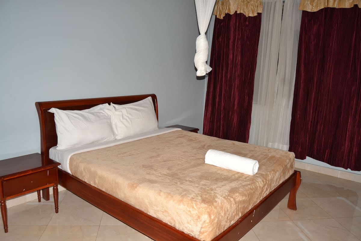 A neatly made bed with a beige blanket, a wooden headboard, and a white pillow.