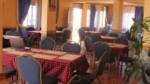 Un espace repas avec des tables recouvertes de nappes à carreaux rouges et blancs, disposées dans une pièce spacieuse où se trouvent des chaises bleues.