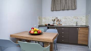Eine kompakte Küche mit Marmorfliesenspiegel, einem Holztisch mit Obstschale und modernen Schränken.