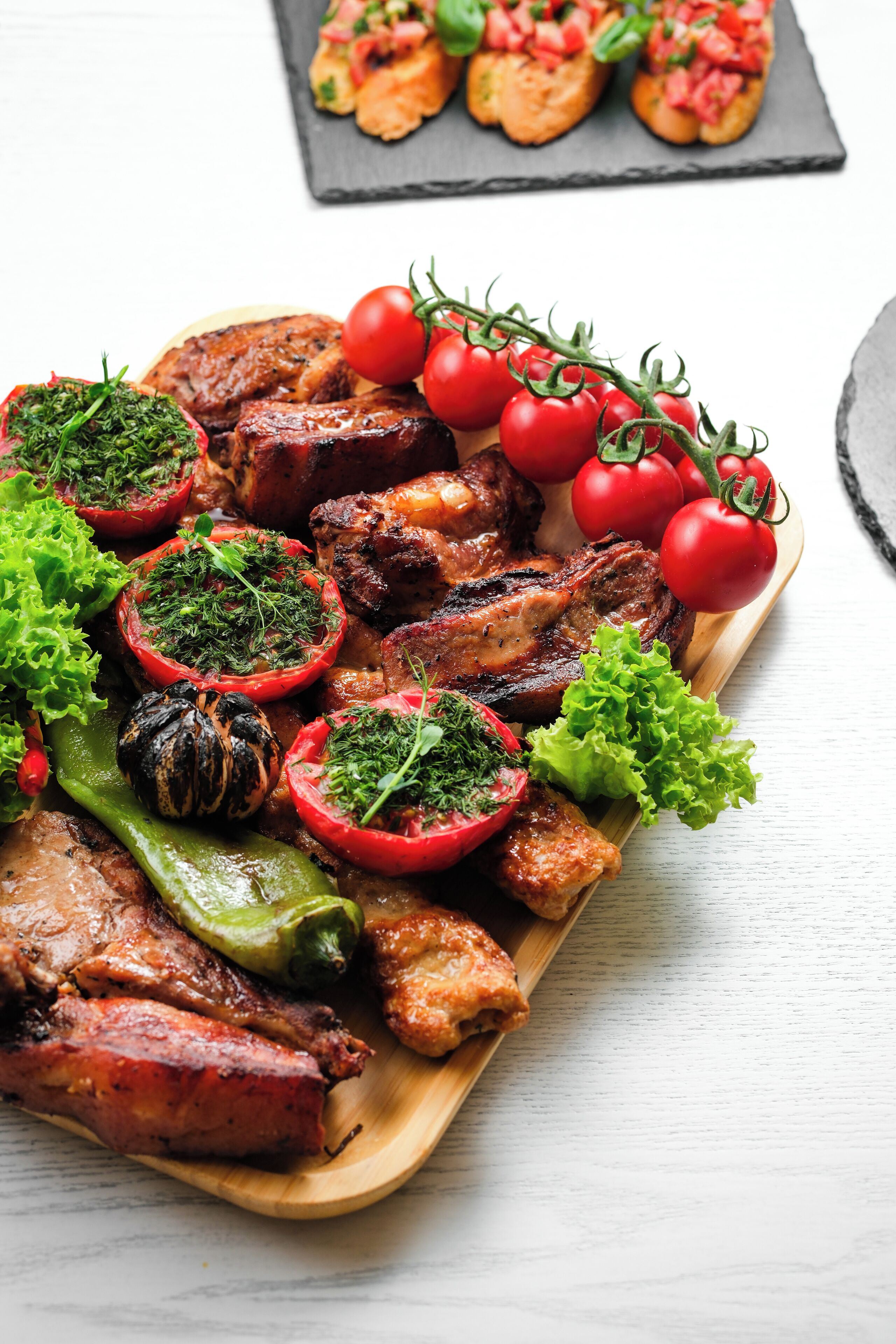 A wooden serving board with grilled meats, tomatoes, and greens.