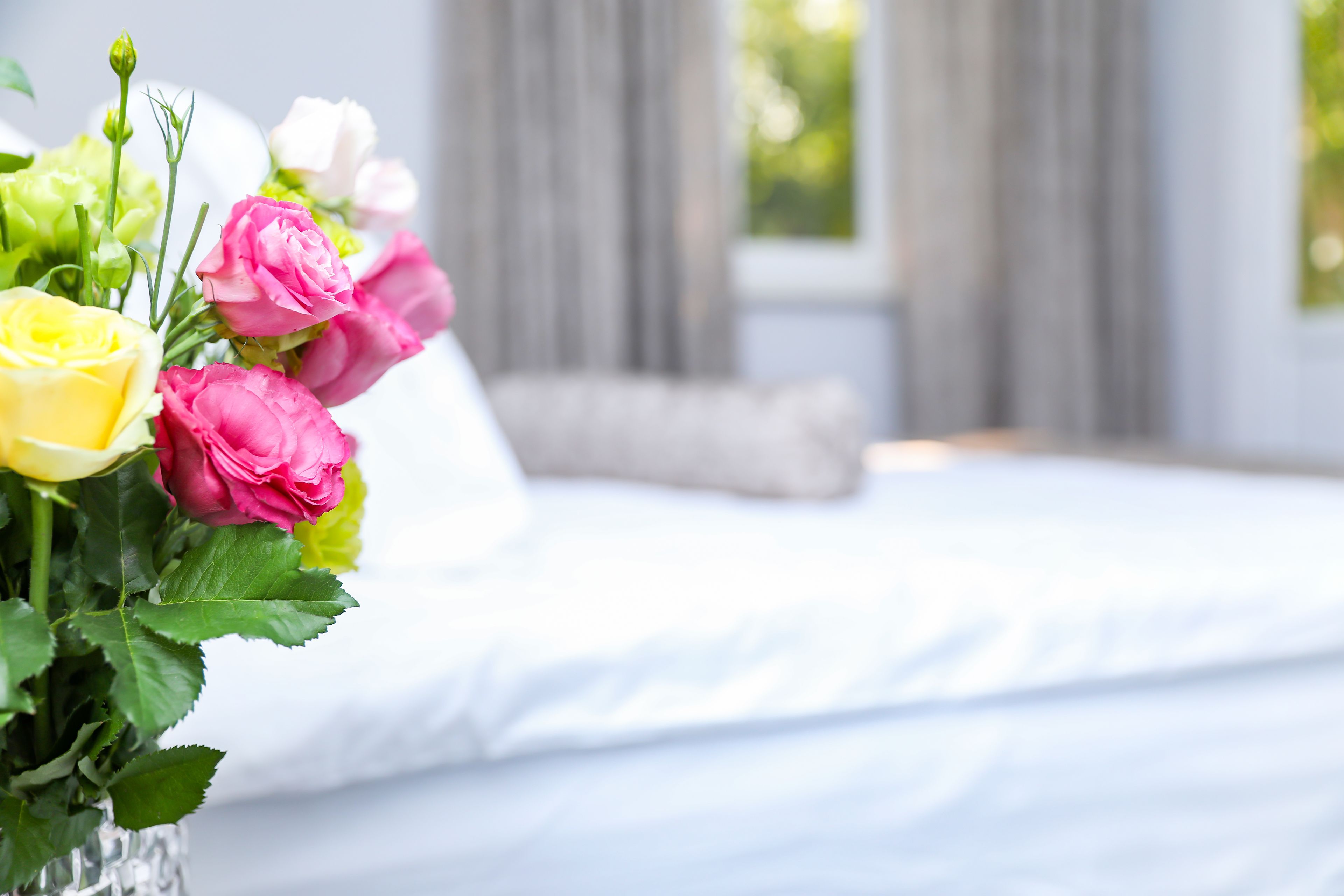 A bedroom with a bed, a vase of flowers, and a window with curtains.