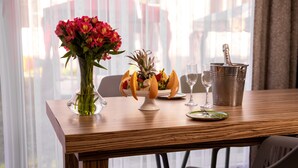 A dining table with a fruit bowl, a vase of flowers, a champagne bottle, and a glass of water.