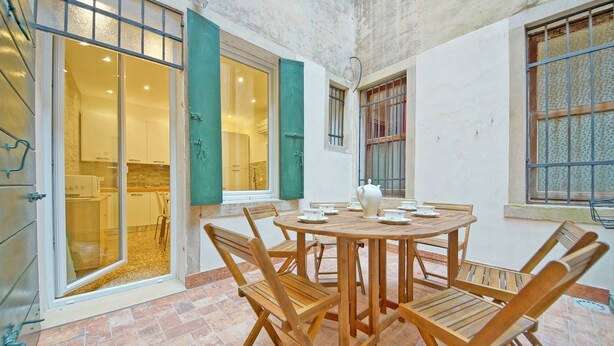 Un coin repas avec une table ronde en bois et des chaises, une cuisine visible à travers des portes vitrées et un sol carrelé.