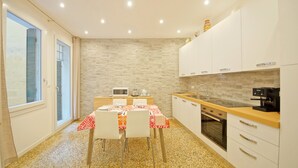 Une cuisine compacte avec des meubles blancs, un four à micro-ondes, une machine à café et une table à manger avec des chaises.