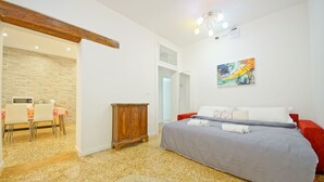 Une chambre à coucher comprenant un lit, une armoire en bois, un coin repas avec des chaises et une table, ainsi qu’un couloir menant à une salle de bain.