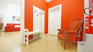Une pièce avec un mur rouge, une porte blanche, un canapé rouge, une chaise en bois, une table blanche et un banc blanc.